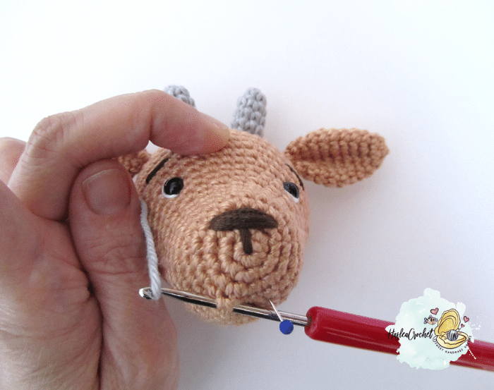 Hand sewing the mouth area of a crochet goat head using a yarn needle and pin for precision