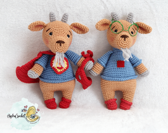 Two finished crochet goat dolls with superhero outfits, including cape, glasses, and violin accessory